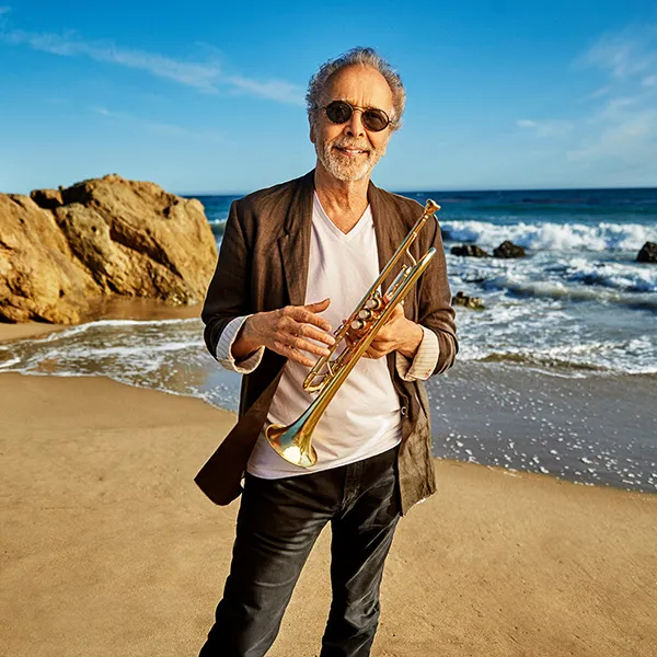 Herb Alpert standing on the beach holding his instrument
