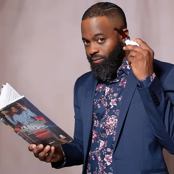 Eddie B. holding a book open with one hand and holding a pipe to his head with the other