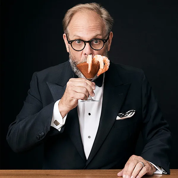 Alton Brown holding a martini glass of shrimp cocktail