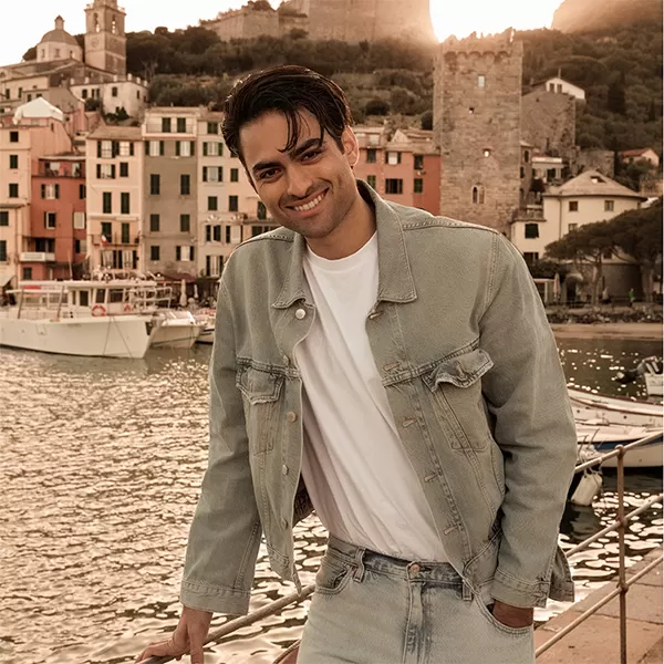 Matteo Bocelli standing outside on a bridge with water and buildings in the background